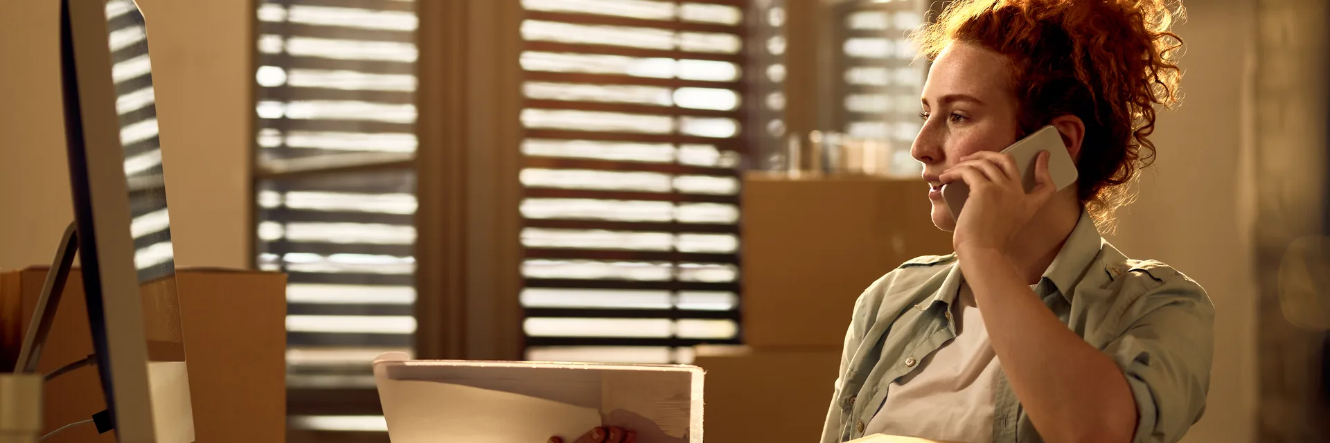 A courier on the phone at a desk surrounded by cardboard boxes and packing materials.