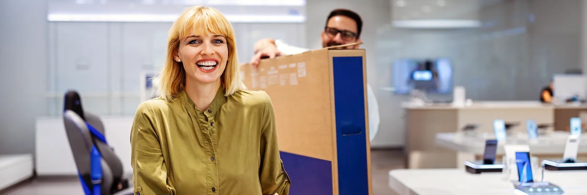 Two people carrying a large boxed television between them.