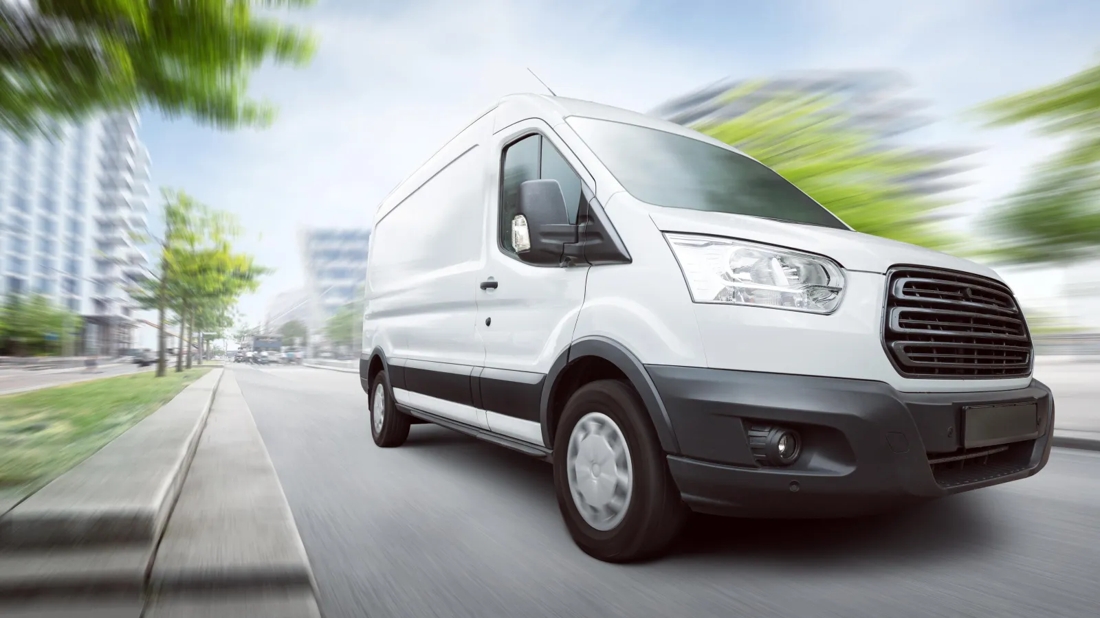 A white cargo van driving along a city street, the background blurred with motion.